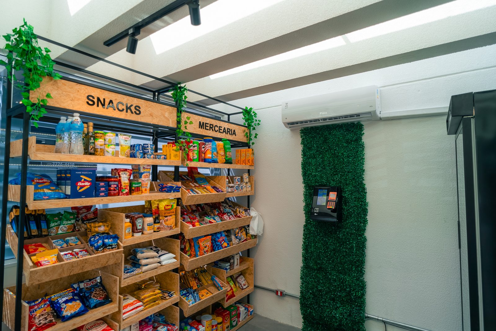Vista completa de uma loja autonoma com parede verde, totem de pagamento e gondolas cheias de produtos