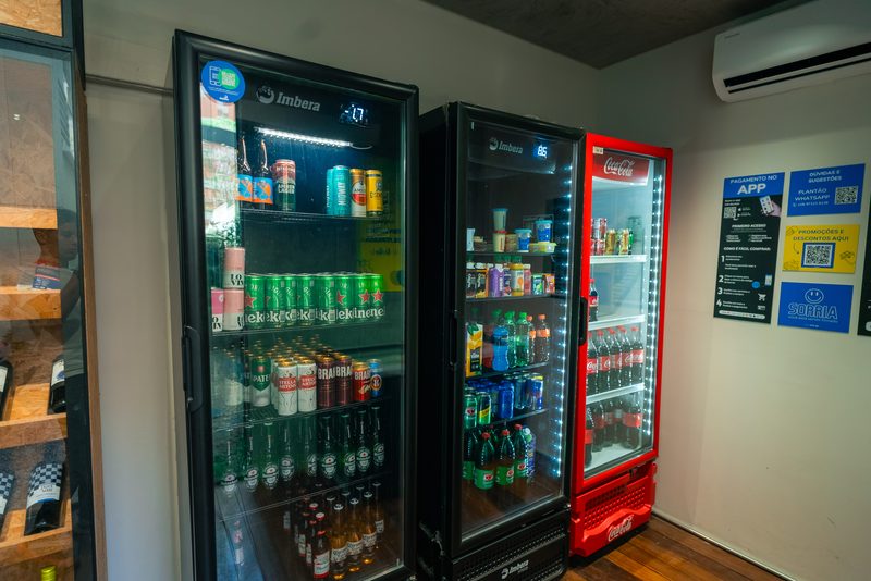 Corredor da loja com geladeiras de bebidas e cartazes com instrucoes de pagamento